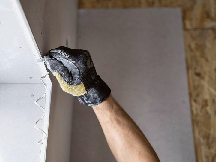 Gloved hand smoothing joint compound onto a wall with a taping knife