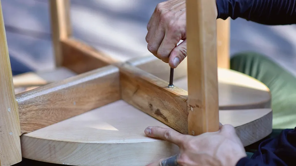 Hands tightening a bolt with a hex key on a wooden stool frame
