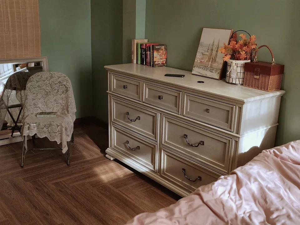 White painted dresser against a green wall in a bedroom with a wood floor