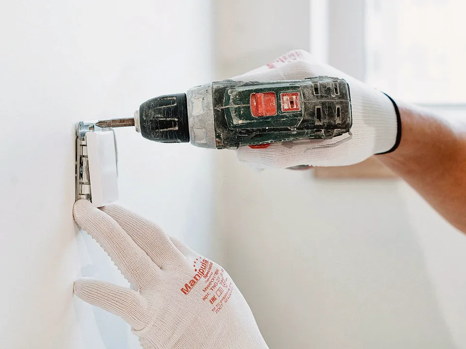 Cordless drill making a pilot hole in a white wall