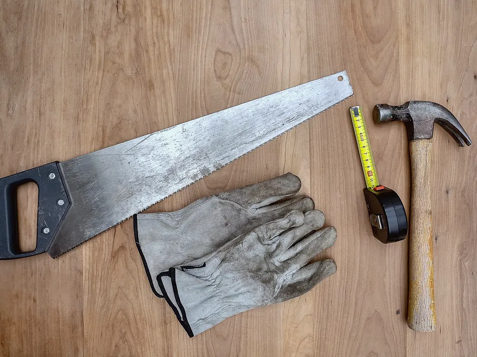 Handsaw, hammer, gloves and tape measure on a workbench