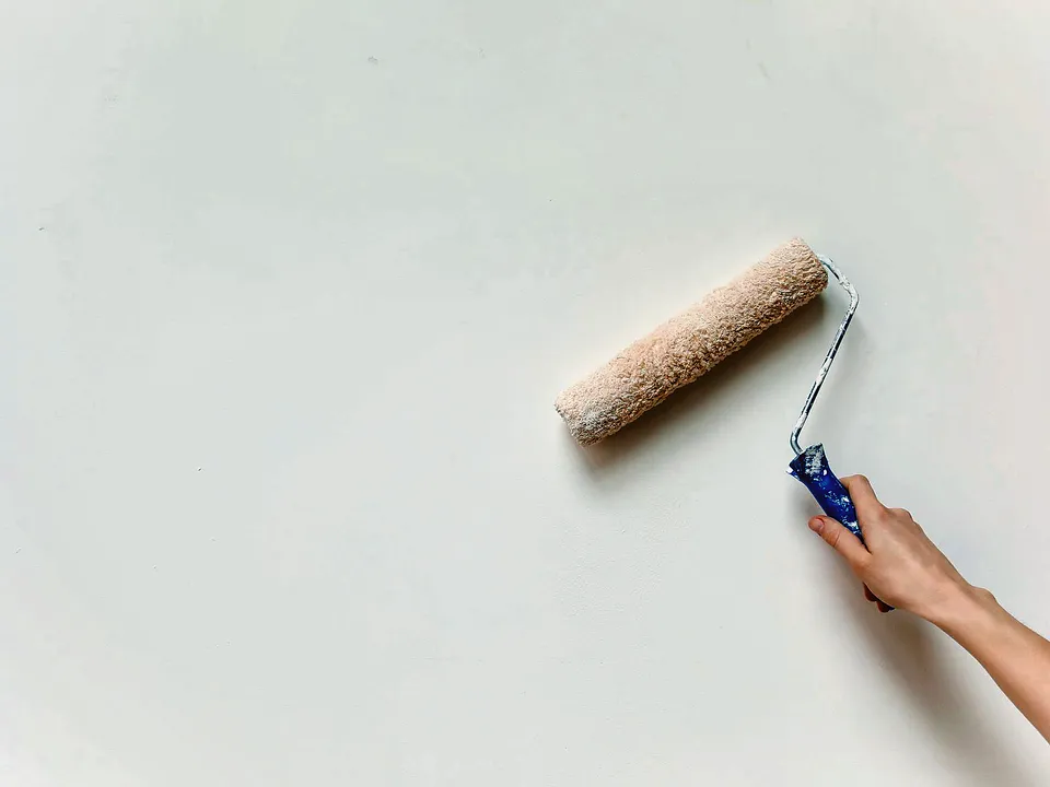 Hand rolling paint onto a white wall with a small roller
