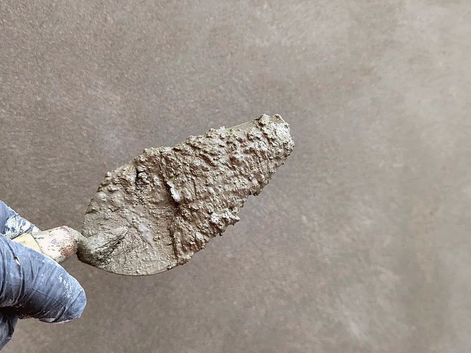 Gloved hand holding a trowel loaded with fresh plaster