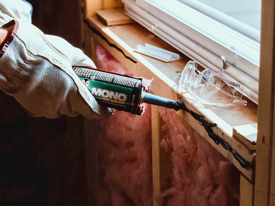 Gloved hand caulking a wood window frame