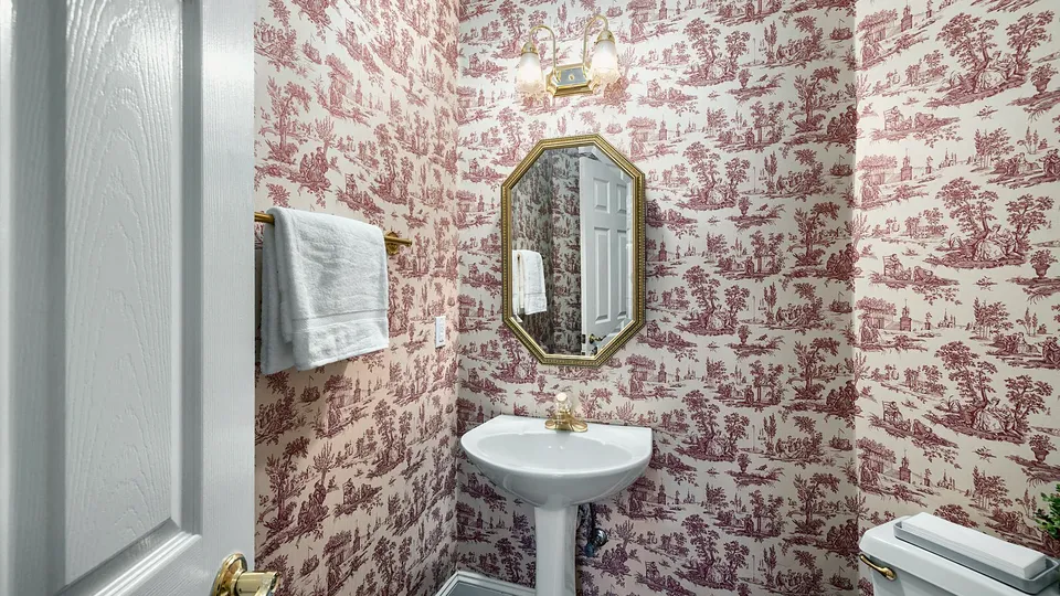 Pedestal sink and round mirror against patterned wallpaper