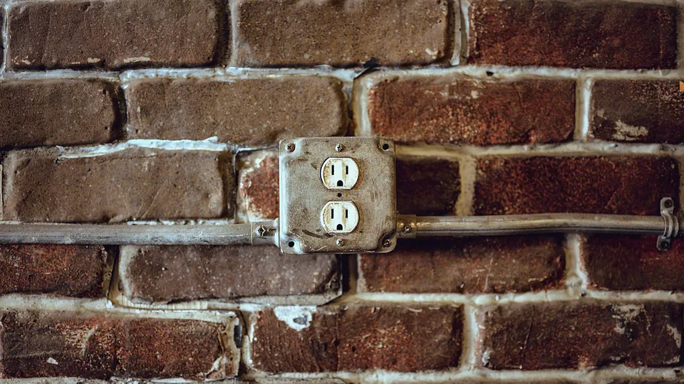 Old two-prong outlet on a painted brick wall