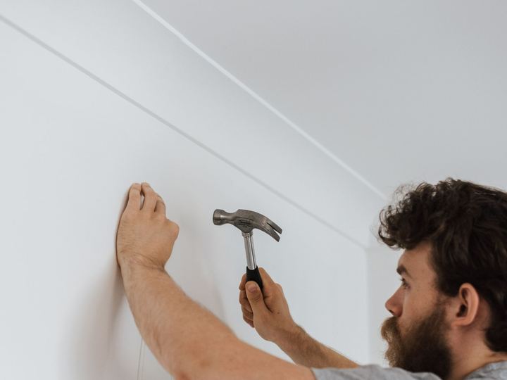 Man tapping a picture hook into a white wall with a hammer