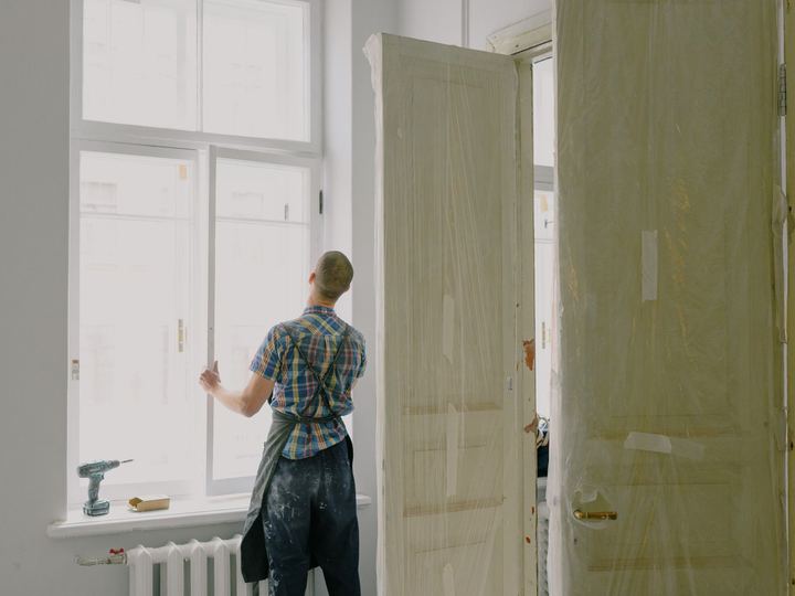 Handyman in a bright room checking a tall window beside two paneled doors