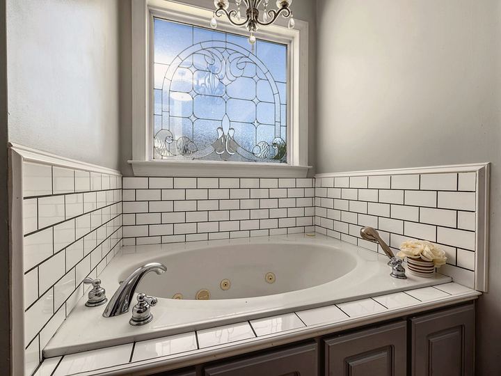 Tub surround with white subway tile and dark grout lines under a leaded-glass window