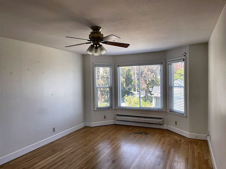 Empty living room with a bay window, ceiling fan and wood floor after a round of small repairs