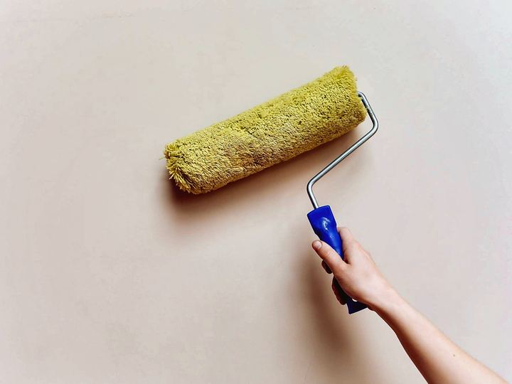 Hand rolling warm off-white paint onto a wall with a yellow roller