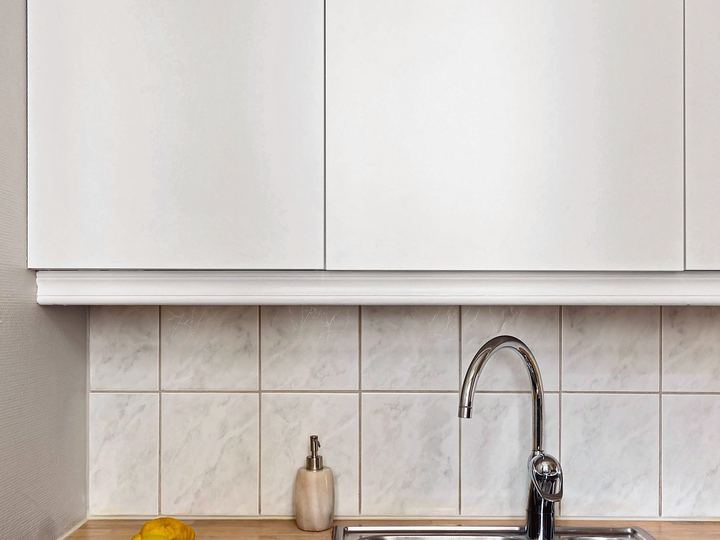 Stainless kitchen sink and faucet below white cabinets