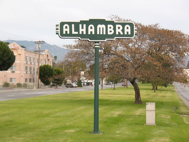 Green Alhambra street sign on a grassy median with trees