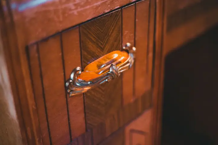 Brass handle on a reddish wood cabinet drawer