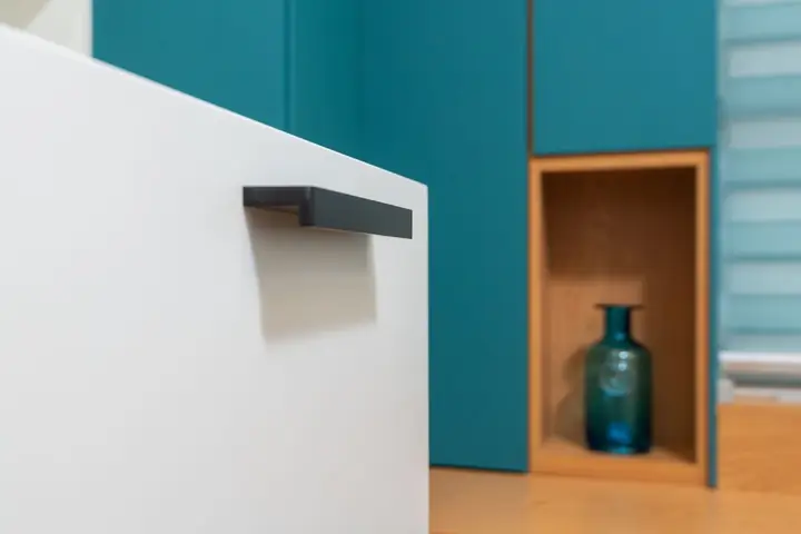 White drawer with a black pull beside teal cabinets