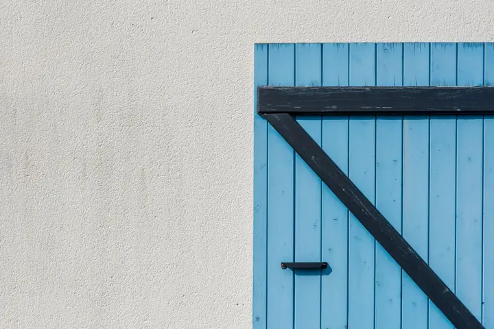 Simple blue wooden door with diagonal black hinge on a textured white wall