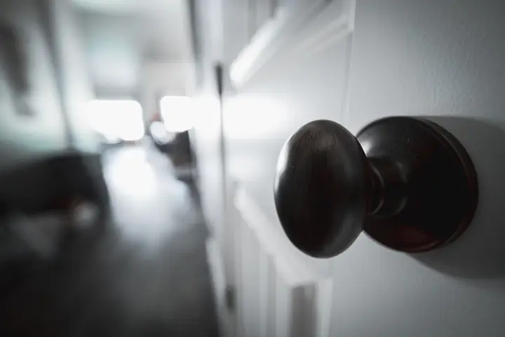 Round metal knob with glare from the light on white wooden door in apartment