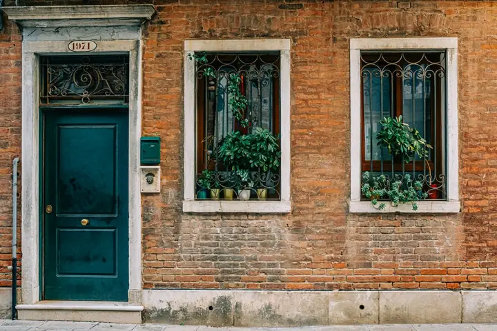 Rustic brick exterior with green door and potted plants on window sills
