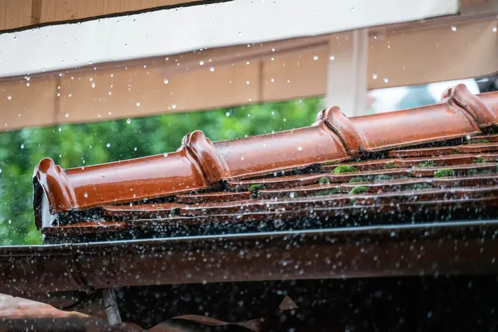 Rain dripping off red clay roof tiles and a gutter