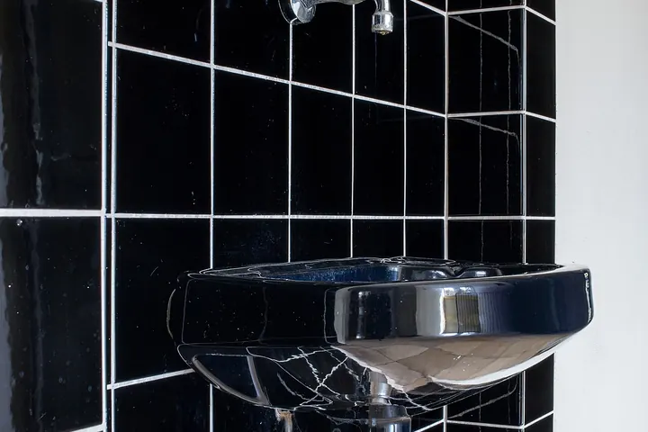 Small wall-mounted sink and faucet on black tile
