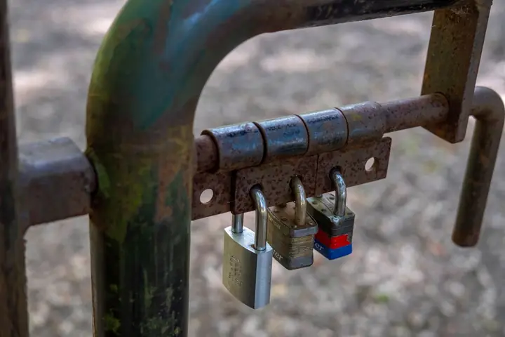 Close-up of a rusty gate secured with three padlocks, symbolizing security and protection