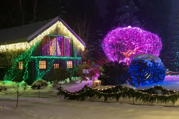 A cottage adorned with colorful Christmas lights in a snowy winter landscape