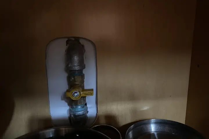 Brass shutoff valve with a yellow handle on the water line inside a cabinet