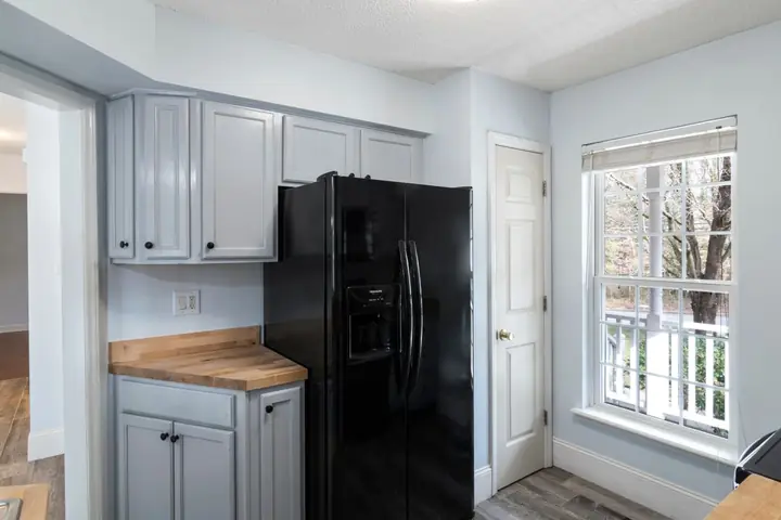 Black refrigerator between gray cabinets near a window
