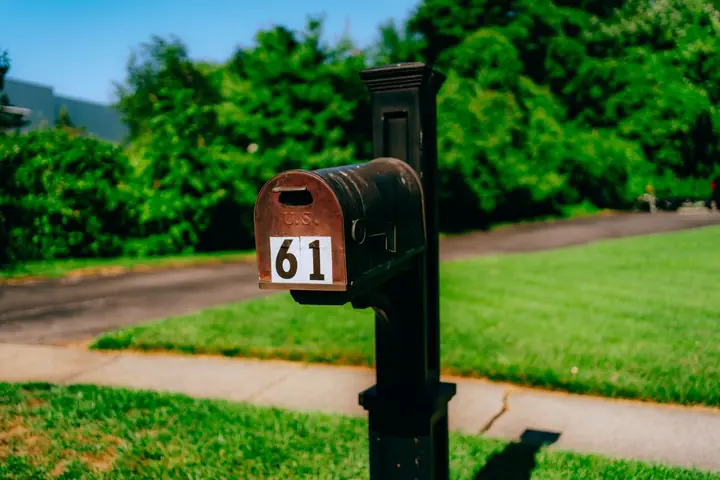A traditional mailbox with number 61 in a rural setting, surrounded by greenery