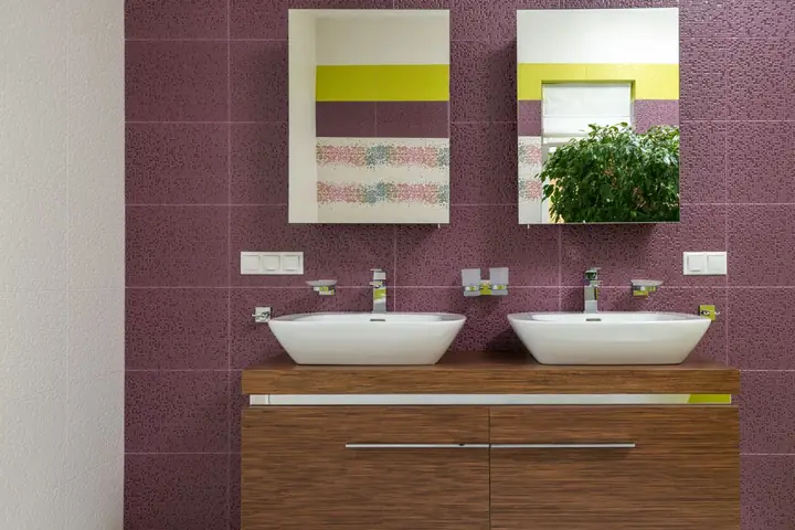 Two white vessel sinks on a wood vanity against purple tile