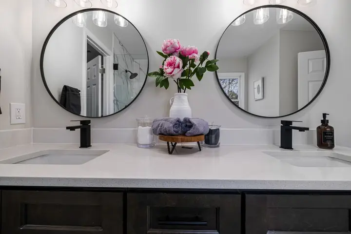 Two round mirrors over a double vanity with black faucets