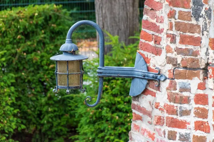 Vintage outdoor lantern mounted on rustic brick wall with green foliage background