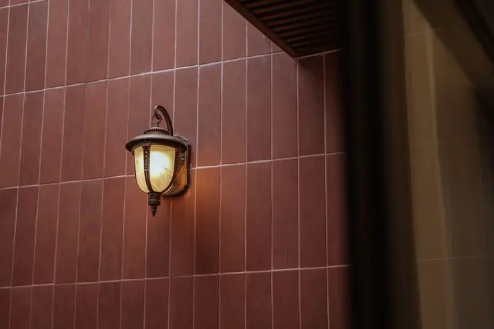 A vintage bronze wall lantern emits warm light against a red brick wall at night