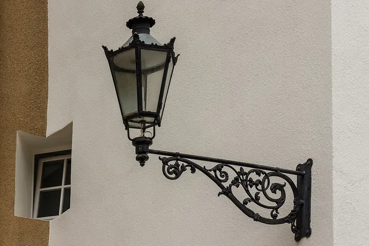 Iron wall lantern on an ornate arm beside a window