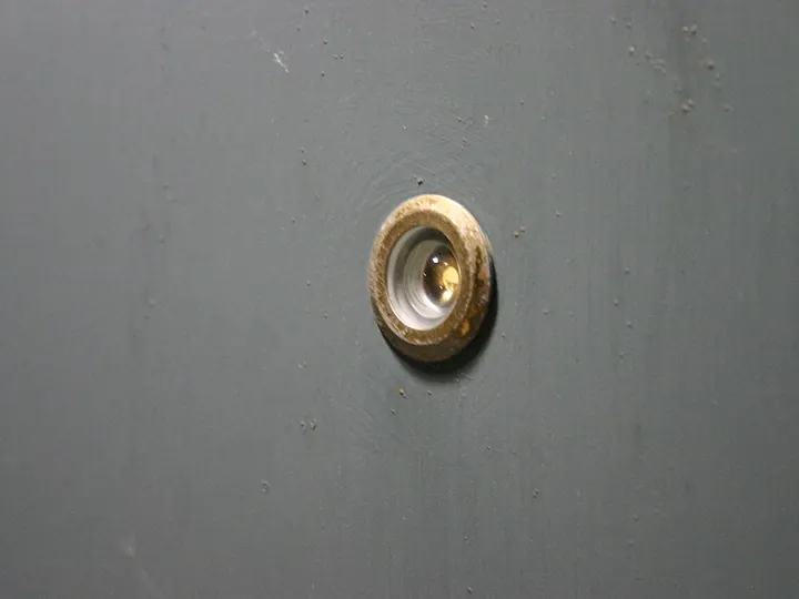 Round brass door viewer set in a gray front door