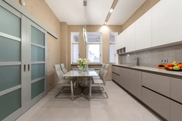 Frosted sliding doors beside a long white kitchen and dining table