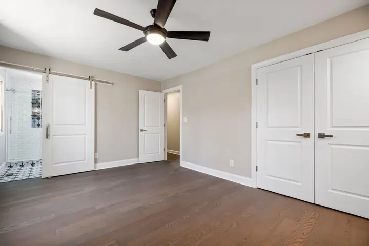 Empty room with a wooden floor, ceiling fan, and sliding barn door