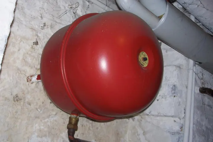Red expansion tank mounted on a basement wall with copper piping
