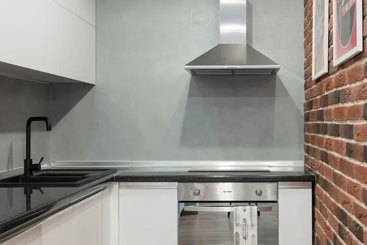 Steel range hood above a cooktop beside a brick wall