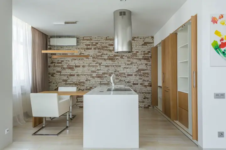 Island range hood over a white counter and brick wall