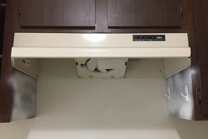 Cream range hood mounted under dark cabinets