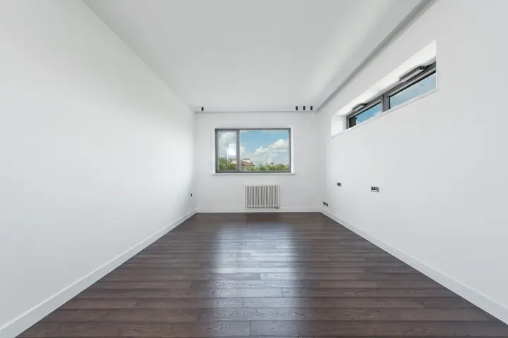 Interior of empty room with white walls and brawn parquet floor in daylight