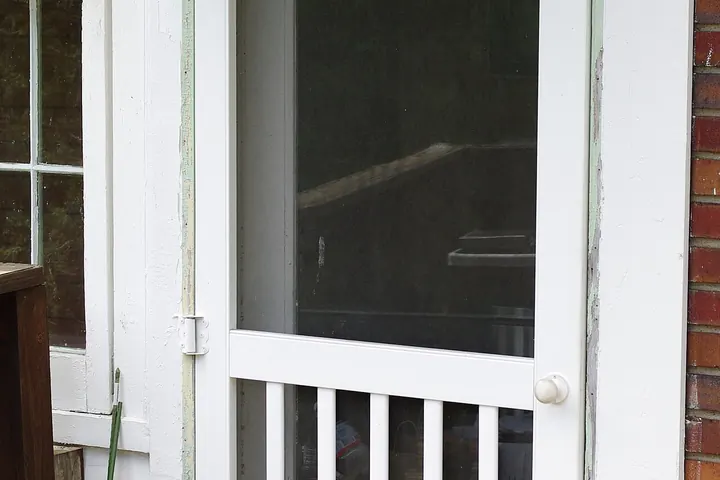 White wooden screen door with a spindle lower panel on a porch