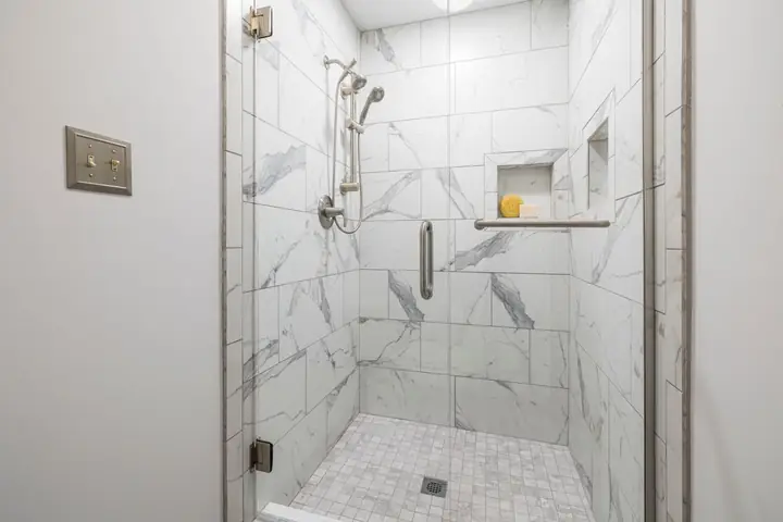 Glass shower with marble tile walls and a wall niche