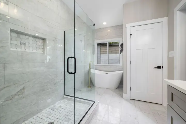 Glass shower beside a freestanding tub in a white bathroom