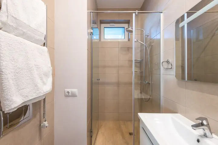 Glass shower beside a white sink and towel warmer