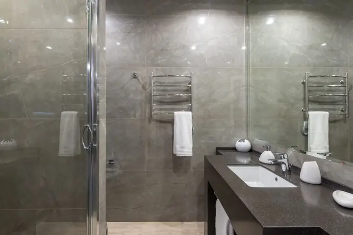 Glass shower next to a dark vanity with chrome towel bars