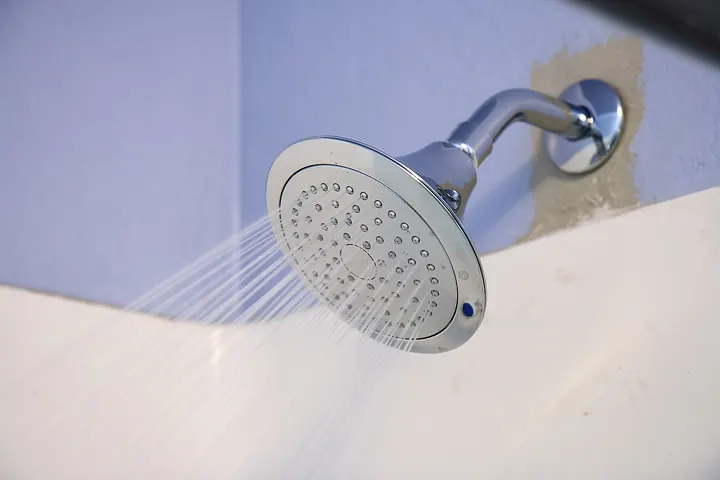 Chrome shower head spraying water against a white wall