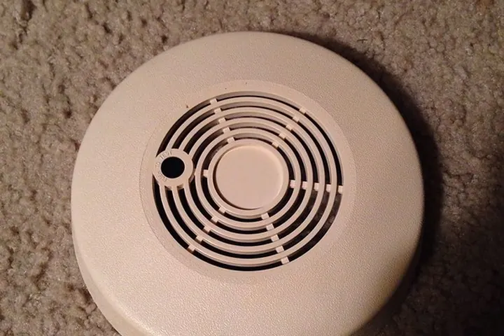 Beige round smoke detector cover lying on a carpeted floor