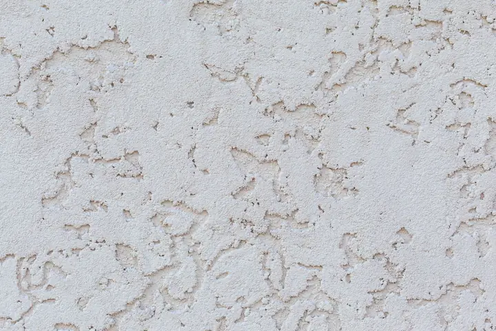 Textured background of white plaster wall with small holes on surface of building